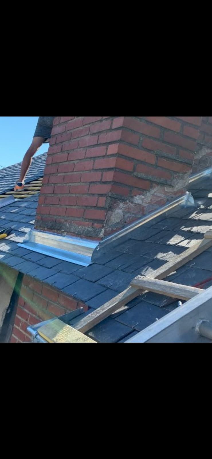 Installation de solins métalliques autour d'une cheminée en briques sur un toit en ardoises.